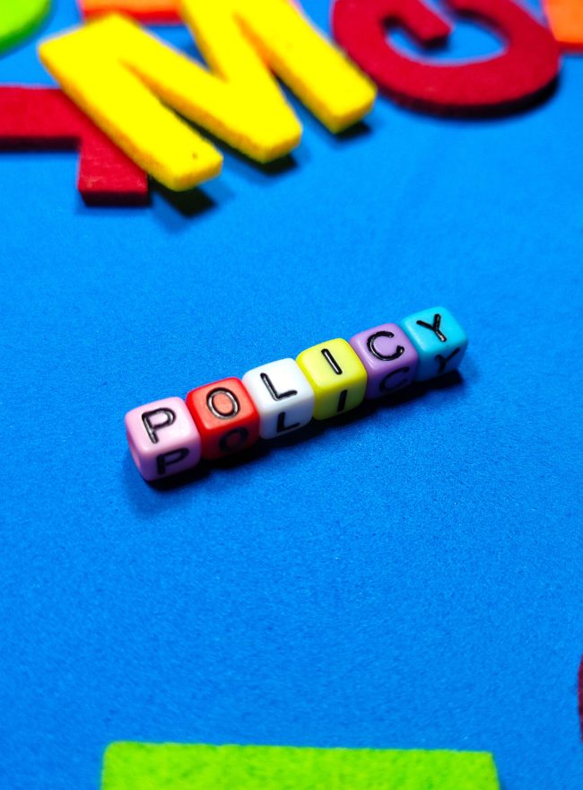 Selective focus.Colorful dice with word POLICY on blue background.Business concept.Shot were noise and film grain.